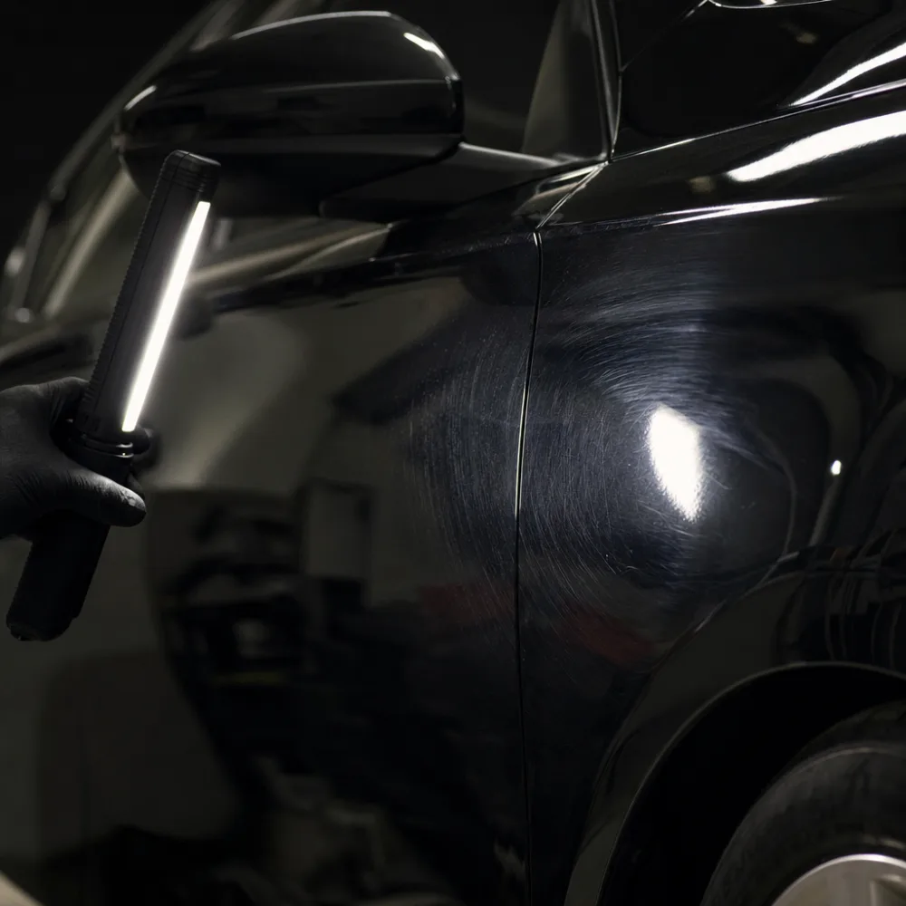 A swirl-marked painted panel shown under an inspection light, before paint correction